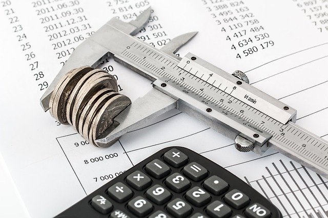 caliper measurement holding coins on top of financial journal with calculator on foreground