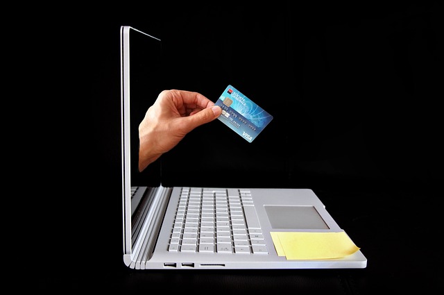 hand with credit card coming out of notebook computer screen